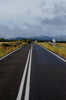 Bulutlarla kaplı dağlara doğru düz bir yol.