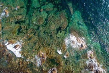 Turkuaz suları olan kayalık bir sahil şeridinin insansız hava görüntüsü.