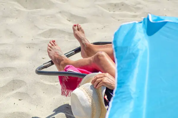 legs of an older woman sunbathing on the beach on a sun lounger, summer vacation concept