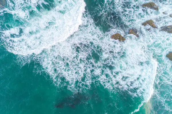 drone aerial view of ocean waves breaking against rocks on the coastline