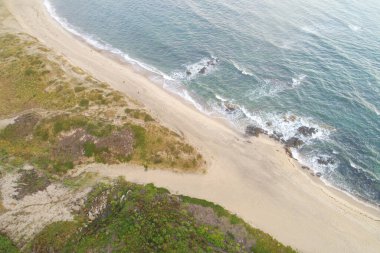 Üç kişinin yaz mevsimi konseptiyle boş bir plajda gezindiği hava manzarası.