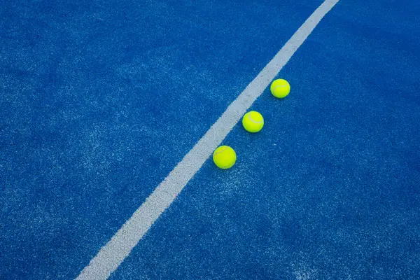 Orta çizginin yakınındaki mavi bir çim kortunda üç raket tenis topu. Seçici odak