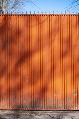 Günbatımında ağaç dallarının gölgesi olan kırmızı metal bir kapı.