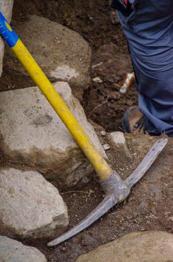 Arkeolojik bir kazıda çalışırken duvara dayanan plastik saplı bir kazma..