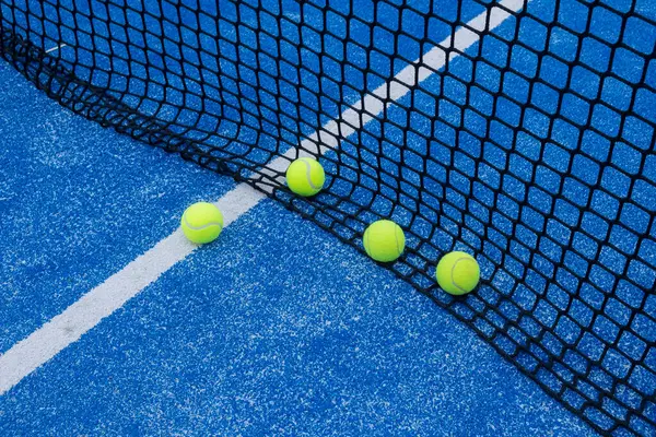 paddle tennis balls by the net of a paddle tennis court