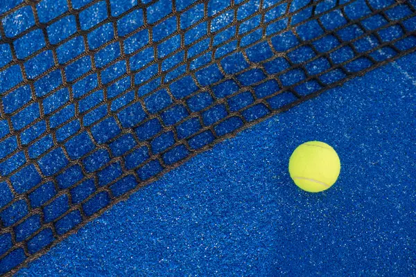 Paddle tennis ball near the net of a blue court. Ball next to the net of a blue paddle tennis court. Ball next to the net of a blue paddle tennis court. Ball next to the net of a blue paddle tennis court.