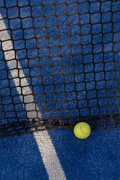 paddle tennis ball in the net of a blue paddle tennis court.
