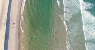 Sahilde sörfçülerin olduğu bir sahilin havadan çekilmiş görüntüsü.