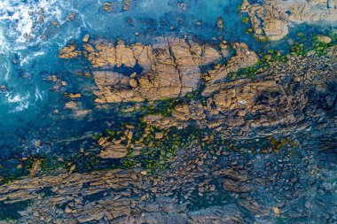 Okyanus kayalıkları üzerindeki hava aracı görüntüsü. Mavi okyanus dalgalarının gökyüzü manzarası uçuruma vuruyor..