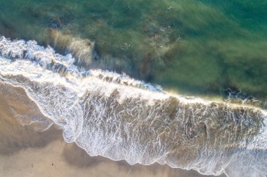 Kumsalda kopan bir dalganın köpüğü, insansız hava aracıyla tepemizde. Havadan yaz manzarası