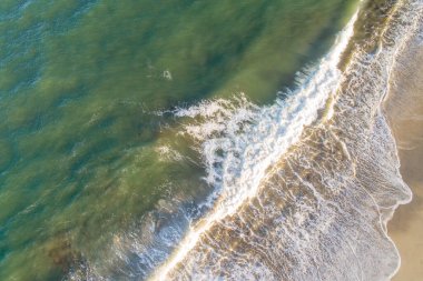 Kumsalda bir dalganın köpüğü kırılıyor, İHA 'lı üst görüntü. Havadan yaz manzarası