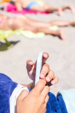 Yazın kumsalda güneşlenirken akıllı telefonunu kullanan bir genç.