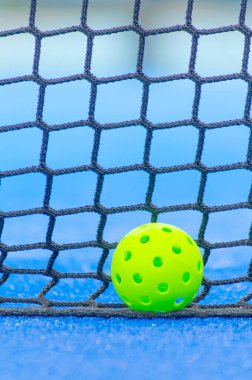 Mavi bir sahanın ağlarının yanında, odaklanamadığı arka planda bir picleball topu