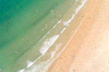 Turkuaz suyu olan bir sahilin zenital hava aracı görüntüsü, sörf okulu öğrencilerinin sörf yapmasını sağlıyor..