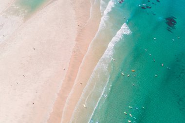 Sörf okulu öğrencilerinin sörf yapmayı öğrendiği turkuaz suyla dolu bir sahilin havadan drone görüntüsü.
