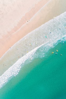 Turkuaz suyu olan bir plajın zenital hava aracı görüntüsü. İnsanlar sahilde yazın tadını çıkarıyor ve sörf yapmayı öğreniyor..