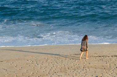 Tanınmayan bir kız şafakta sahilde yürüyor.