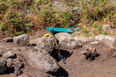 Arkeolojik bir kazıda kayaların yanında bir kürek ve el arabası.