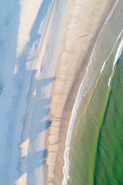 Yazın gündoğumunda bir kumsalın kıyısı insansız hava aracından görüldüğü gibi, zenital görüntü.