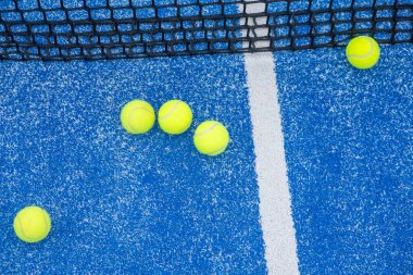 Mavi bir raket tenis kortunda, ağın yanında beş topun görüntüsü