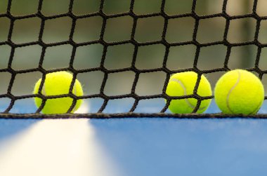 Mavi bir raket tenis kortunun yanında üç top, odaklanamadığı arka plan.