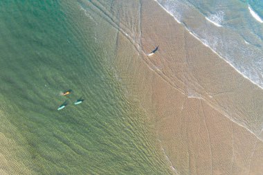 Sahil kenarında sörf tahtaları olan dört sörfçünün hava görüntüsü.
