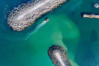 Bir limanın girişinde seyreden bir gemi dalgakıran tarafından korunuyor, insansız hava aracı ile havadan görüntüleniyor..