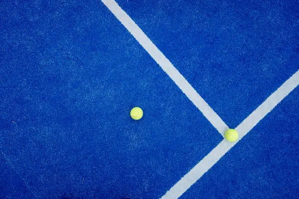 Mavi raket tenis kortunun üst görüntüsü ve dokusu ve iki sarı top. Yapay çim kürekleri mahkeme yüzeyi.