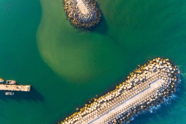 Yazın günbatımında dalgakıranlar tarafından korunan bir limanın girişinin insansız hava aracı görüntüsü.