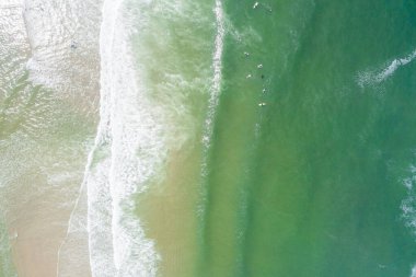 Yazın, sahilde dalgalarda sörf yapan insanların olduğu bir sahilin zenital manzarası. Drone fotoğrafçılığı