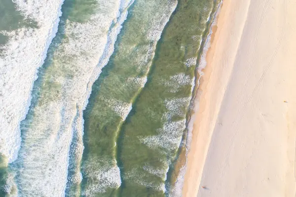 Yaz mevsimi, güneşli bir günde yeşil bir deniz suyunun güzel dalgalarını denizlere serer. İHA 'nın üst görüntüsü. Deniz manzaralı, doğa manzaralı. Dalgalar ve kumsal kumları ile aydınlık deniz.