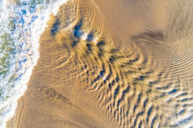 Zenital hava aracı görüntüsü yaz mevsiminde bir sahil kıyısında dalgaların akışını gösteriyor.