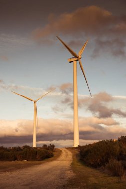Gün batımında bir dağda iki yel değirmeni türbini, altın saat. Yenilenebilir enerji kavramı