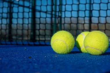 Raket sporları. Mavi raket tenis kortunda, ağın yanında üç raket tenis topu..