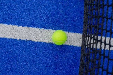 Paddle tennis ball next to the net of a blue artificial grass paddle tennis court. clipart