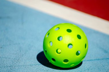 Mavi kort yüzeyinde izole edilmiş yeşil bir picleball topu.