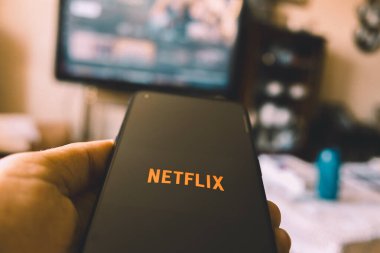 Madrid, İspanya 08-10-2024: Netflix uygulamalı akıllı telefonu olan bir kişinin eli, oturma odasında televizyonun önünde oturuyor.