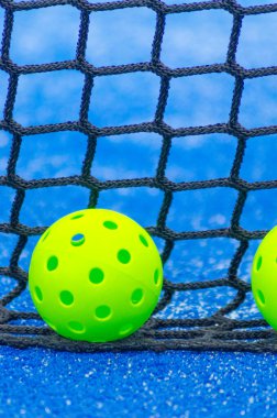 Saha yakınında iki yeşil yankesicilik topu, turşu kulübünde, mavi arka planda.