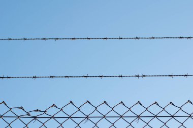 Üzerinde dikenli teller olan bir tel örgünün mavi gökyüzü manzarası