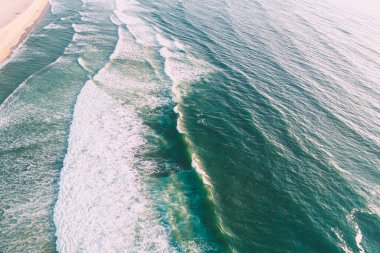 Deniz dalgaları köpüren bir plajın kıyısına geliyor, şafakta insansız hava aracıyla havadan zenital görüş.