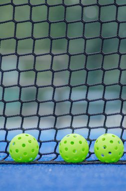 Pickleball sahasında kalenin yanında üç plastik yeşil top, raket spor konseptinin arka planı.