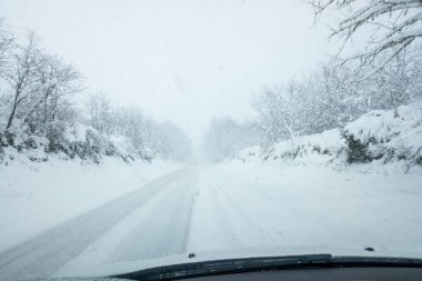 Bir arabanın içindeki kar yağışı sırasında kırsal bir yolun görüntüsü. Yoğun kar yağışı sırasında araba yolda, sürücü koltuğunun perspektifinden görülüyor.