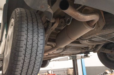 Bakım ve teftiş için oto tamirhanesinde hidrolik asansörde kaldırılan arabanın alt görüntüsü. Garajdaki araç çalışmaya hazır..