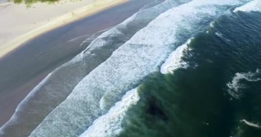 İnsansız hava aracı yazın bir kumsalda hareket eder, dalgalar köpük yapar.