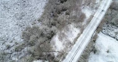 Beyaz bir minibüs, karlı bir yolda, hava aracı görüntüsünde dikkatle sürüyor.