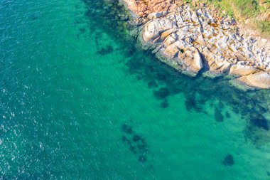Turkuaz deniz suyuyla kayalık kıyı şeridi, insansız hava aracı ile havadan manzaralı.