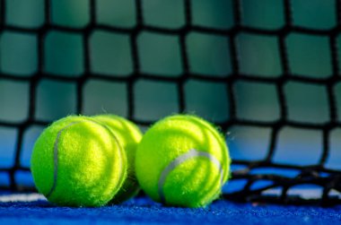 Mavi bir padel kortunda ağların yanında üç raket tenis topu, raket sporu konsepti arka plan