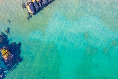 Temiz turkuaz su ve kıyı kayaları, kayaların soyut hava görüntüsü ve berrak deniz desenleri havadan aşağı insansız hava aracı görüntüsü