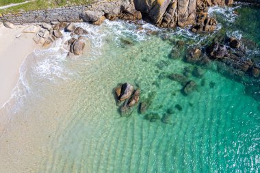 Kıyı sahili kayalıkları kumlu bir plajda. Gök mavisi turkuaz deniz, hava aracı üst görünümü.