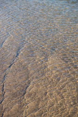 Temiz su vasıtasıyla görülebilen kum desenlerinin kumlu kumsalda akan sığ ve berrak su